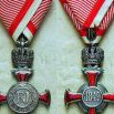 Obě strany stříbrného Záslužného kříže s korunou na válečné stuze